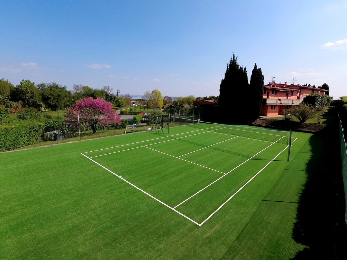 Campo da tennis in erba sintetica con prato verde e villa